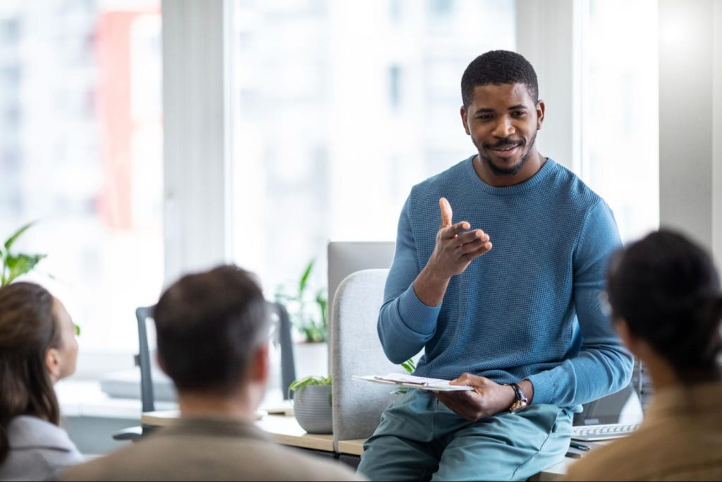 Empreendedorismo social - homem negro fazendo uma apresentação diante de outras pessoas em um escritório