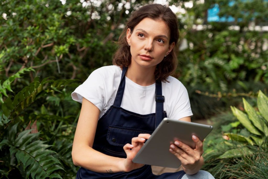 O que é empreendedorismo social - jovem mulher segurando um tablet em uma área aberta com diversas plantas.